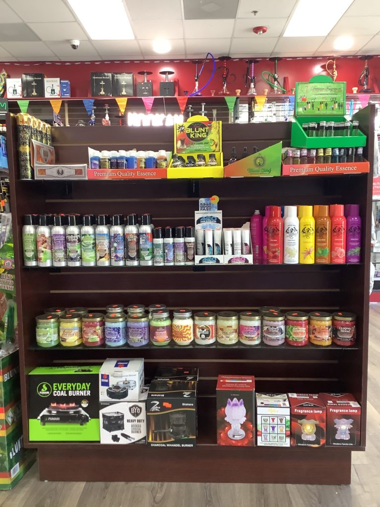 Store shelf displaying a variety of smoking accessories, herbal products, sprays, and hookah supplies in a colorful retail setup.